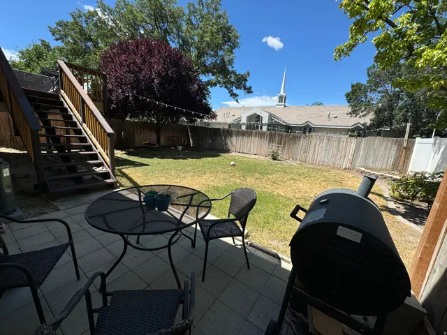 Paved patio area with a wooden privacy fence, mature trees, and an exterior staircase