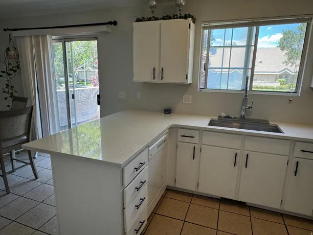 Kitchen featuring quartz countertops, white cabinetry with black hardware, a stainless steel sink with a high-arc faucet, and tile flooring