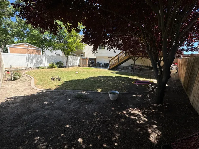 Spacious backyard featuring a manicured lawn, a raised wooden deck with stairs, a mature shade tree, and a concrete garden border