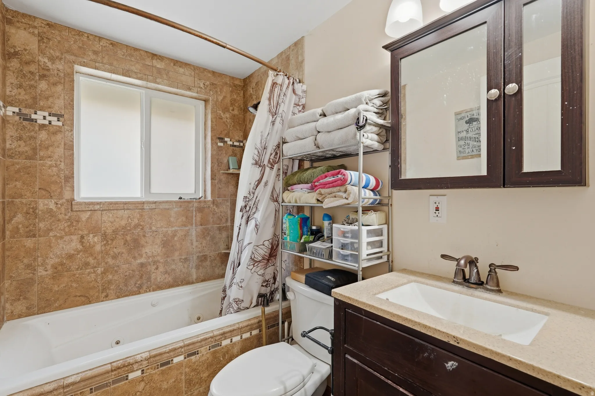 Bathroom featuring a tiled bathtub surround with an inset window, a dark wood-finish vanity with an integrated sink, bronze-finish faucet, and a wall-mounted medicine cabinet with a mirror