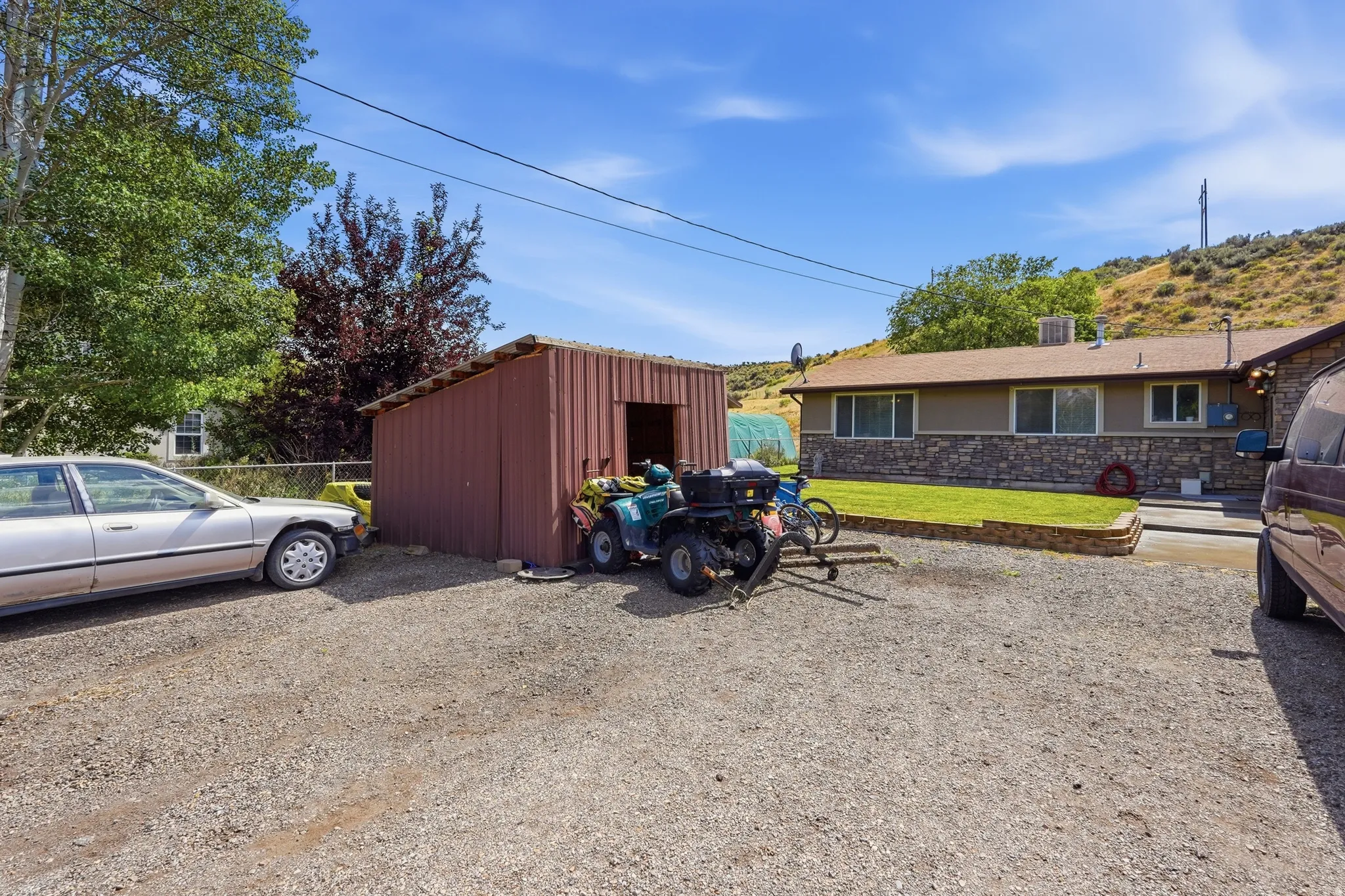 Gravel driveway with a red metal storage shed and a single-story residence featuring a stone facade