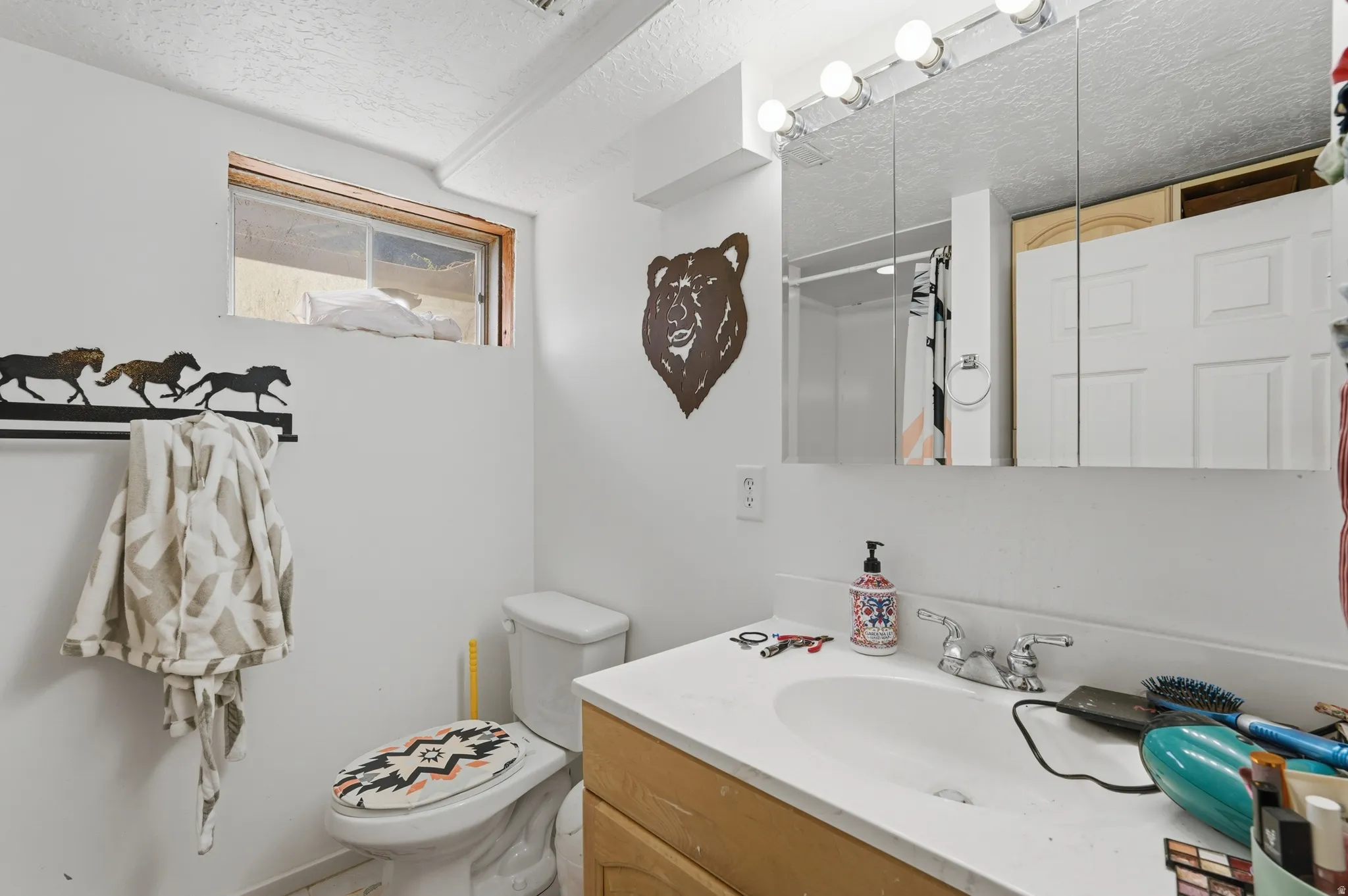 Bathroom featuring a single vanity with light-colored countertop, wall-mounted mirror with integrated lighting, and a window for natural illumination