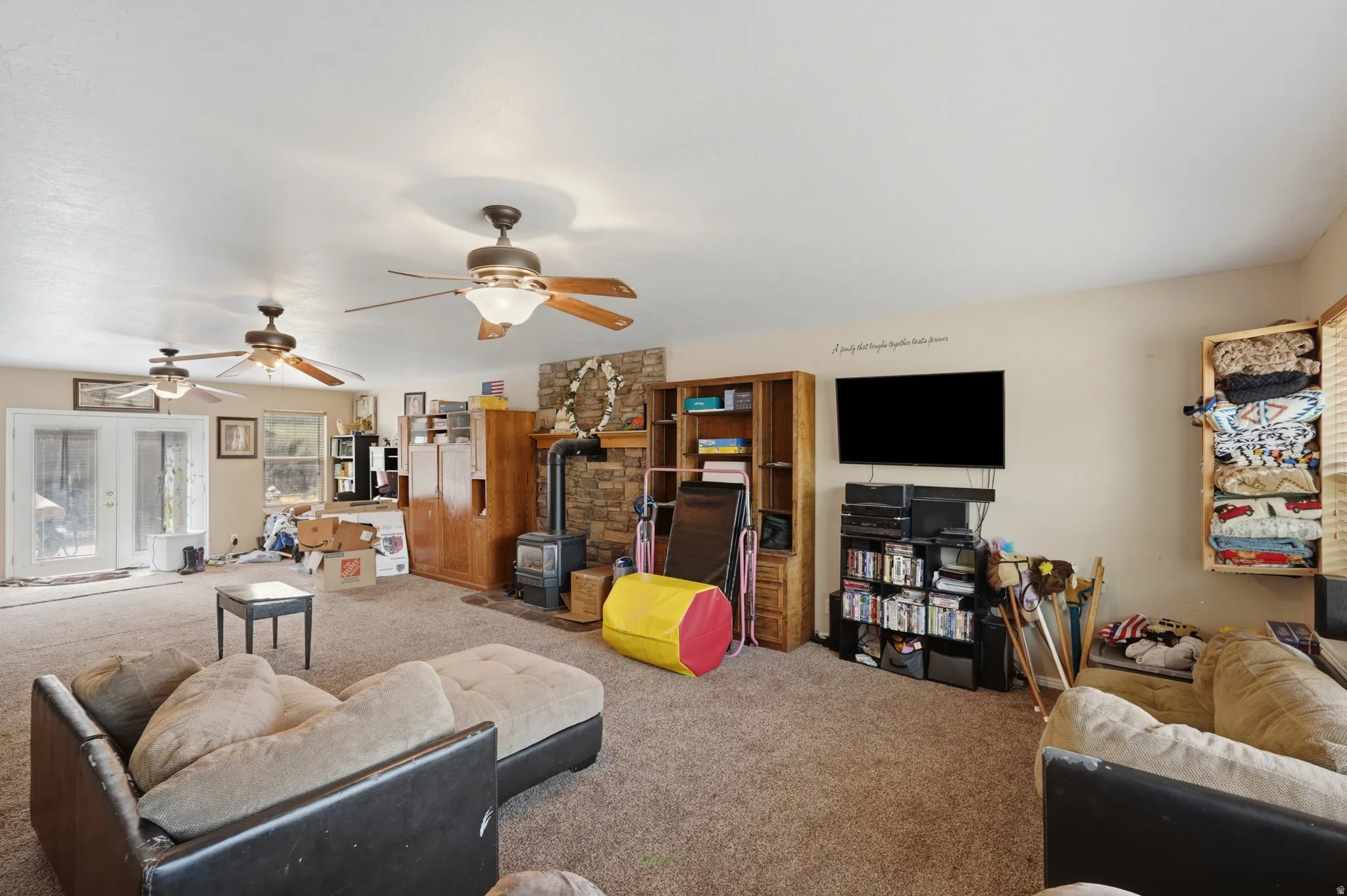 Spacious living area featuring carpet flooring, multiple ceiling fans, and double French doors providing outdoor access