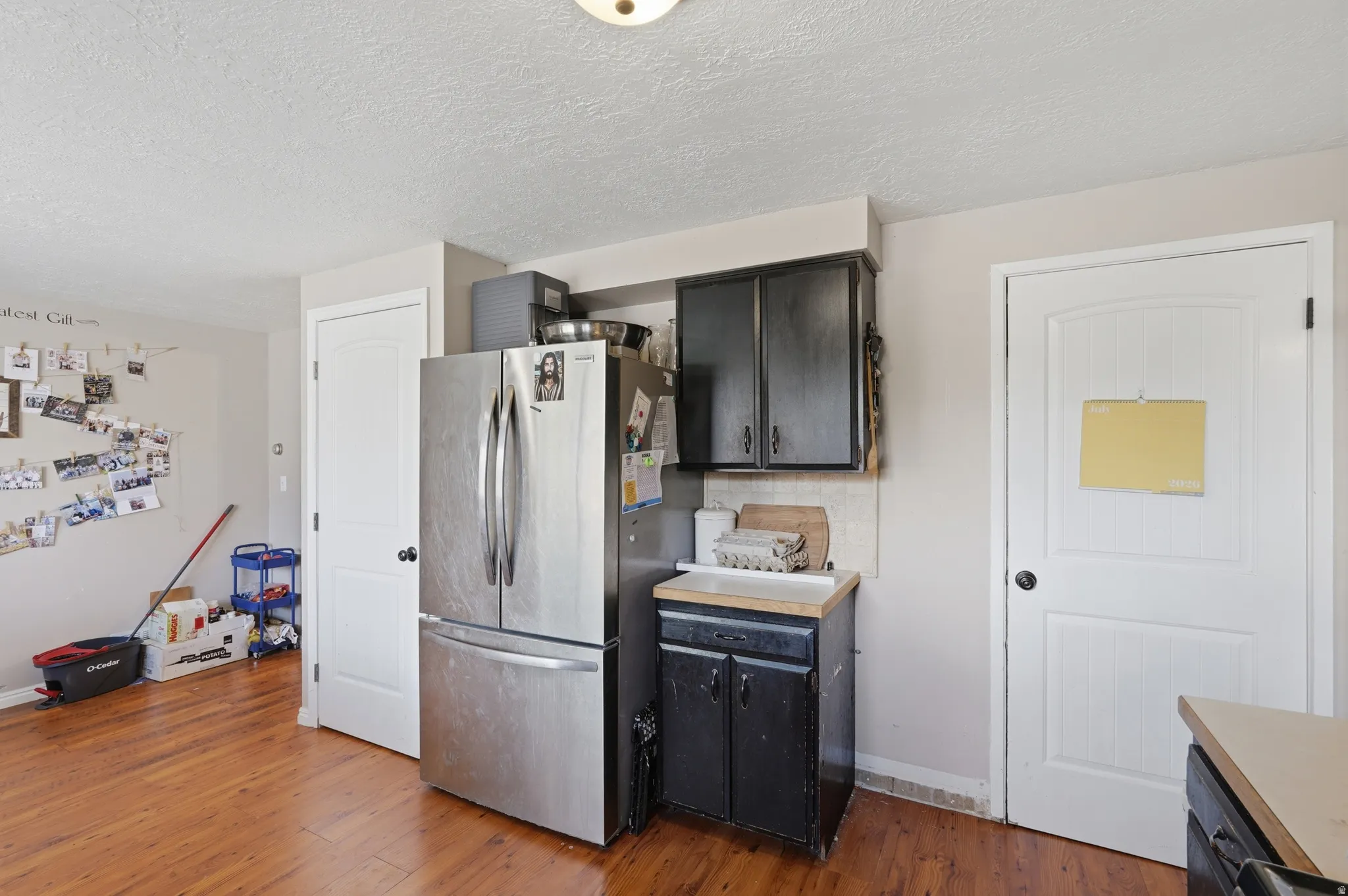 Kitchen area featuring wood-finish flooring, a stainless steel refrigerator, and dark cabinetry