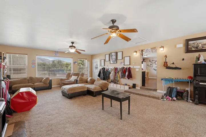 Spacious living area featuring neutral-toned carpeting and walls, multiple windows with horizontal blinds, and two ceiling fans with light fixtures