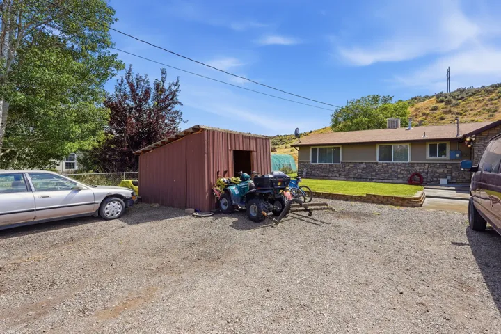 Gravel driveway with a red metal storage shed and a single-story residence featuring a stone facade