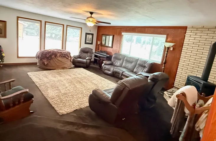 Spacious interior featuring a wood-burning stove with a brick surround, wood paneling, and multiple windows
