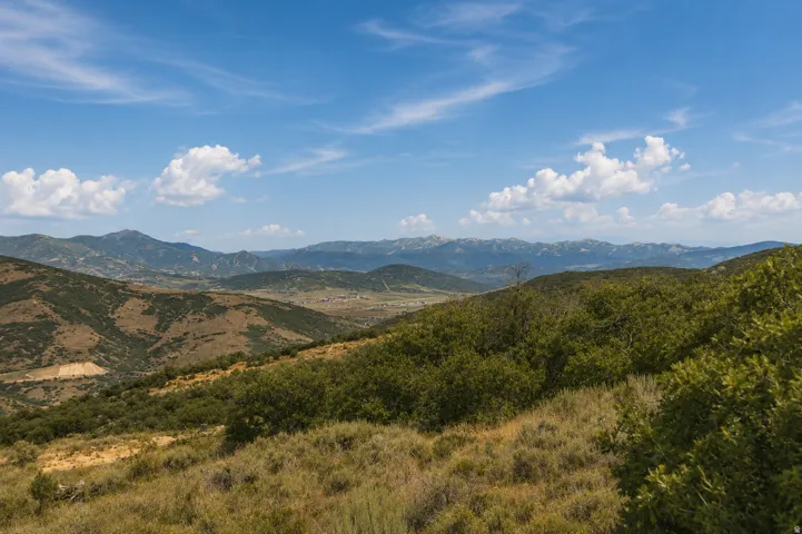 Expansive mountainous terrain featuring varying elevations, natural vegetation, and distant valley