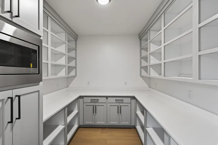 Walk-in pantry featuring extensive open shelving, perimeter countertops, built-in lower cabinetry, a built-in microwave, and wood-finish flooring