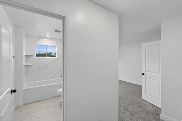 Full bathroom featuring a window above the tub, built-in shelving, white tiled flooring, and a white tub with white tiled surround
