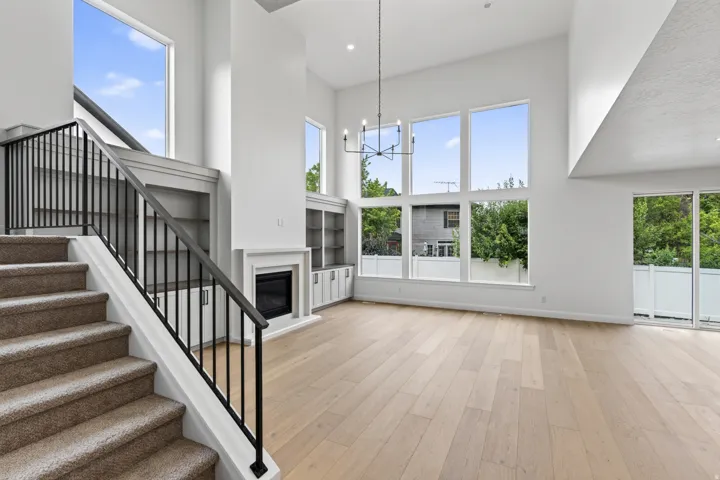 Spacious interior featuring a carpeted staircase with black iron railing, wood-finish flooring, a contemporary fireplace with mantel, built-in shelving, and large windows