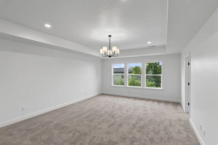 Spacious room featuring neutral carpeting, white walls, and a tray ceiling with recessed lighting