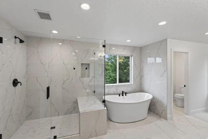 Spacious bathroom featuring a freestanding soaking tub with matte black fixtures, a walk-in shower with a built-in bench and matte black hardware, and large format marble-look tile flooring and walls