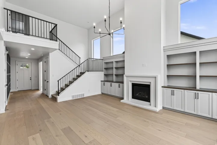 Open-concept living space featuring wood-finish flooring, a contemporary fireplace with a white mantel, and built-in shelving with lower cabinetry