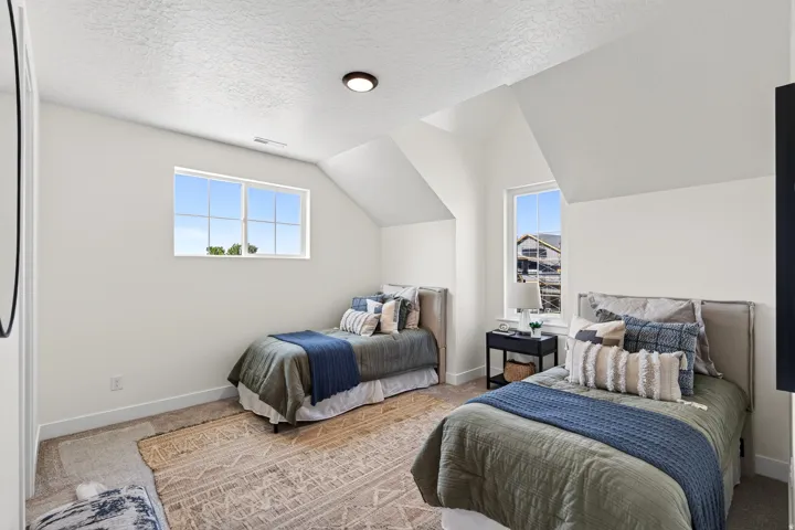 Bright bedroom featuring two windows, neutral carpeting, and sloped ceilings