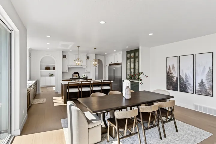 Open-concept kitchen and dining area featuring light wood-finish flooring, recessed lighting, a built-in kitchen island with seating, a sliding glass door, and a dedicated beverage station with built-in appliances