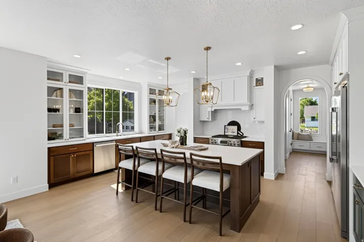 Gourmet kitchen featuring a substantial island with seating, stainless steel appliances, light wood-finish flooring, white shaker cabinetry with glass fronts, and a built-in window seat