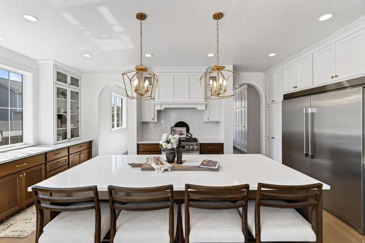 Spacious kitchen featuring a large central island with seating, pendant lighting, stainless steel appliances, white upper cabinetry, and wood-finish lower cabinetry