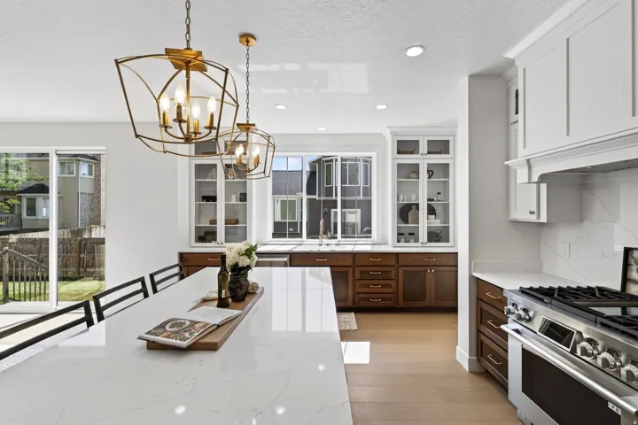 Kitchen featuring a large central island with a light-toned countertop, dual gold-finish pendant lights, light wood-finish flooring, white upper cabinetry, and dark wood-finish lower cabinetry