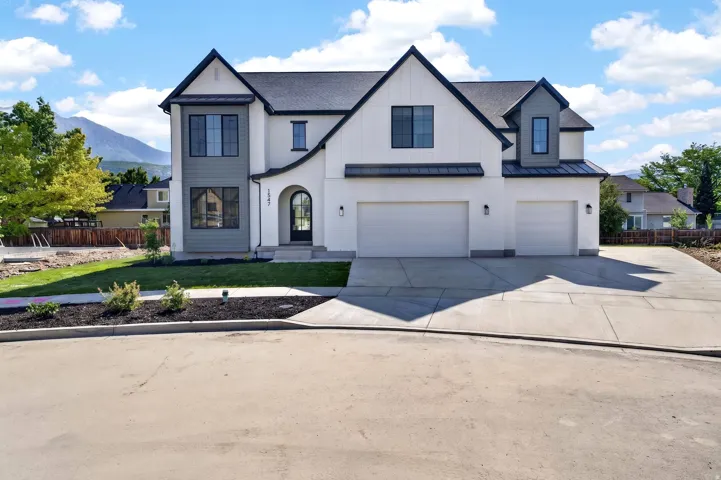 Modern architecture featuring a two-car garage, contrasting exterior finishes, arched entry door, black window frames, and a dark shingled roof