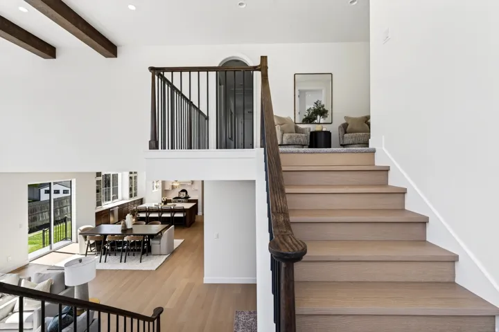 Multi-level interior featuring wood-finish flooring, white walls, dark wood-tone exposed beams, an open-concept dining area, and a kitchen with dark wood-tone cabinetry