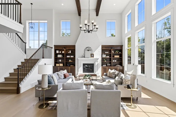 Two-story living area featuring a white brick fireplace, built-in dark wood shelving, wood-finish flooring, and a grand staircase with wrought iron balusters