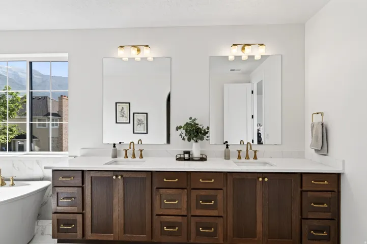 Double vanity with wood-finish cabinetry and brass hardware, featuring white countertops and undermount sinks