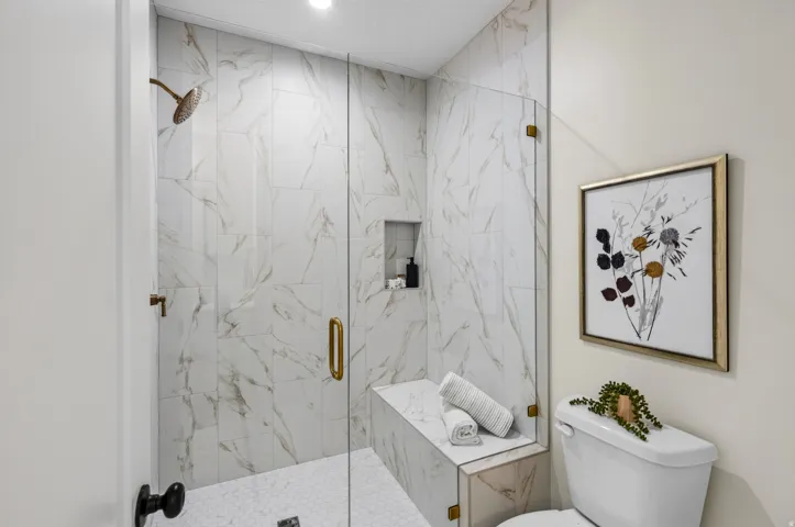 Walk-in shower featuring a frameless glass enclosure, a built-in bench, and a recessed niche