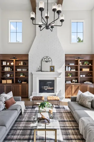 Vaulted living space featuring a white brick fireplace with a classic mantel, built-in wood-finish shelving, and a prominent dark metal chandelier