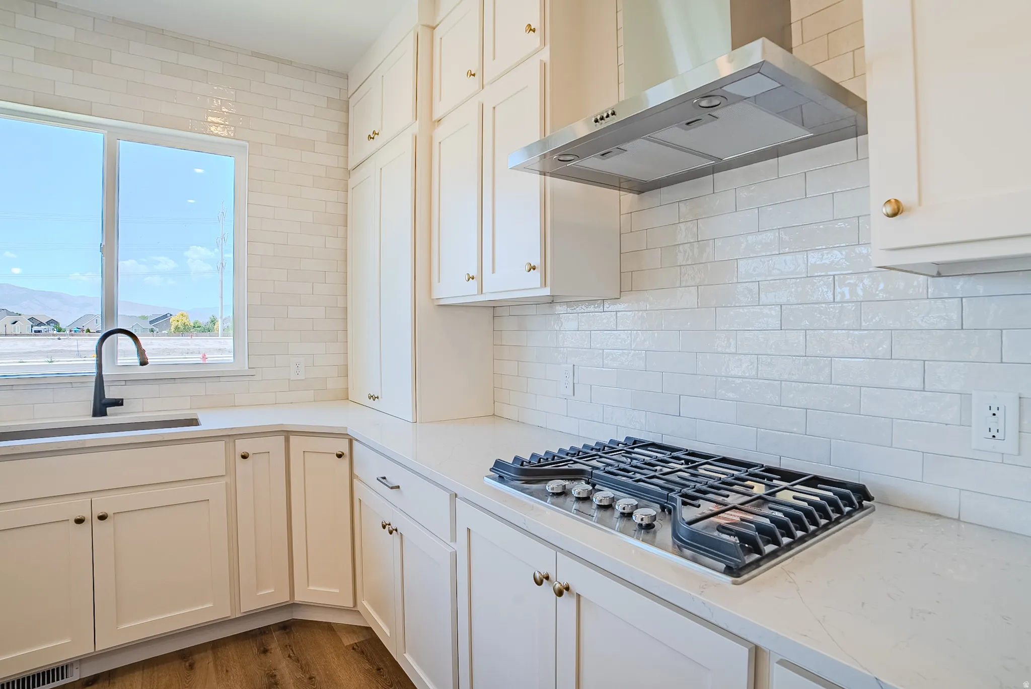 Kitchen featuring white cabinetry, quartz countertops, a stainless steel range hood, a stainless steel gas cooktop, and a white subway tile backsplash