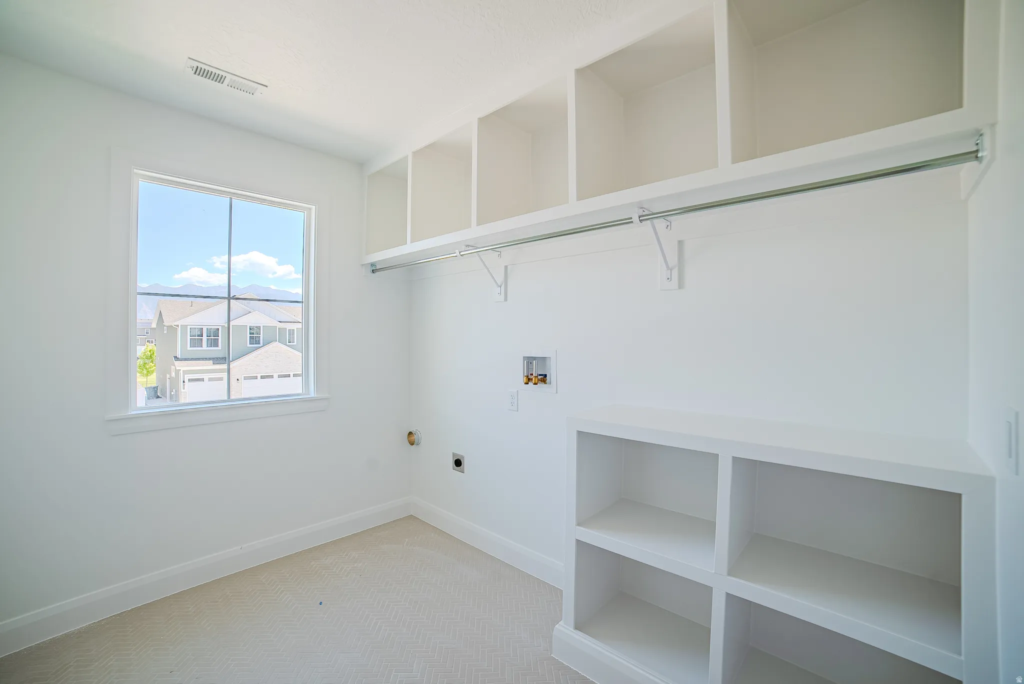 Bright utility room featuring a large window, extensive built-in shelving, a clothes hanging rod, and essential appliance hookups