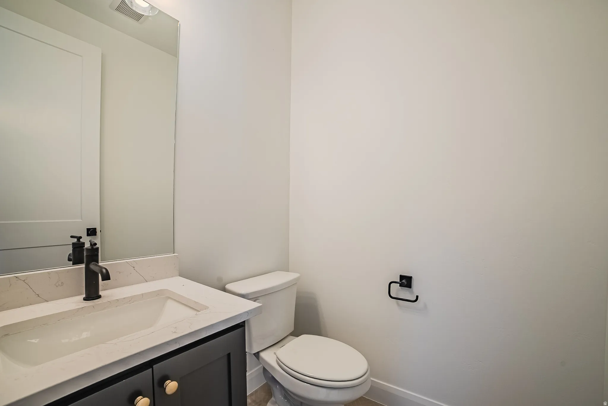 Modern bathroom featuring a dark grey vanity with gold-tone hardware, an integrated sink with a light-toned countertop, a black faucet, and a wall-mounted mirror