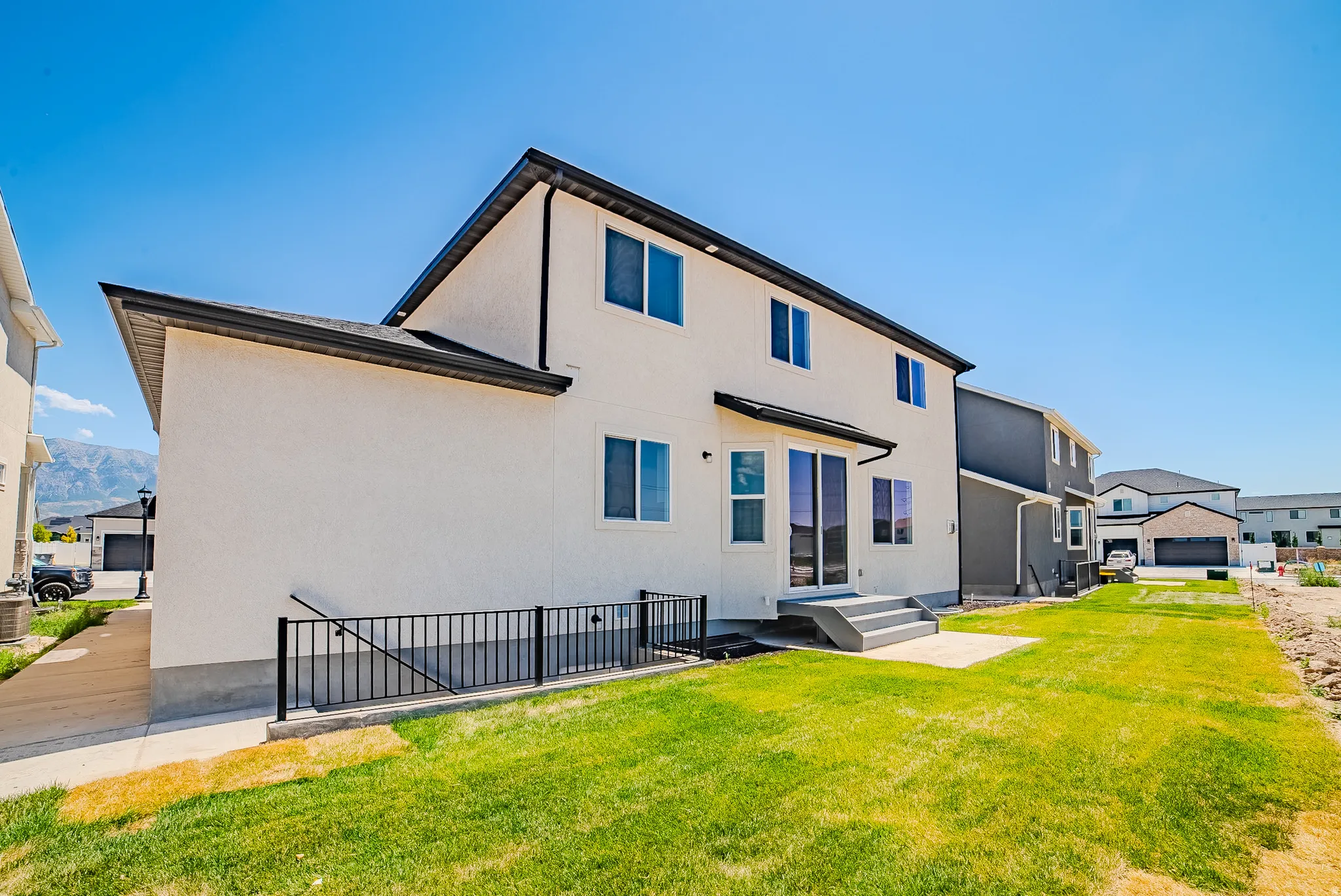 Rear exterior featuring a stucco finish, multi-pane windows, a black roofline, and sliding glass doors leading to a concrete patio and a grassy yard