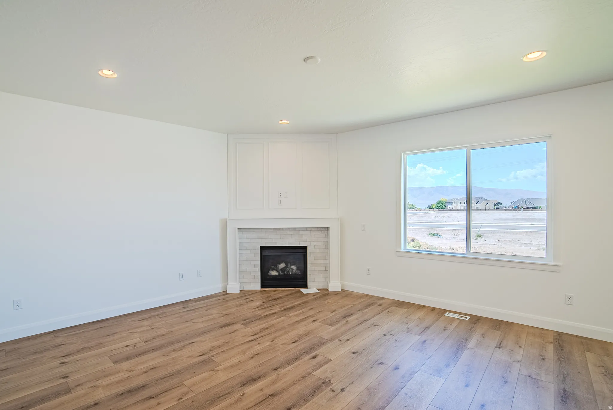 Living area featuring wood-finish flooring, a white mantel, and a fireplace with a light-tiled surround