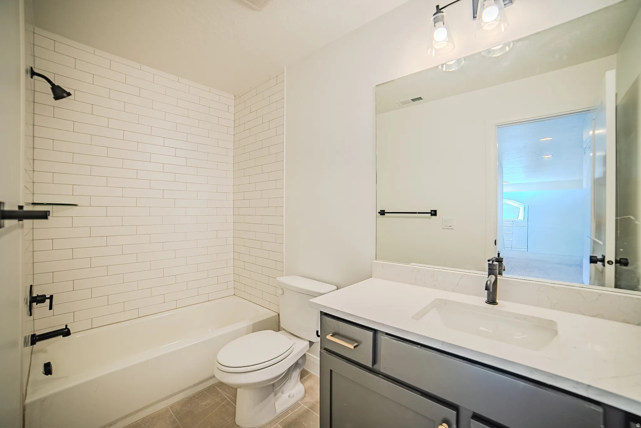 Bathroom featuring a subway tile shower surround, matte black fixtures, a white vanity countertop, and a vanity with gray cabinetry and gold-tone hardware