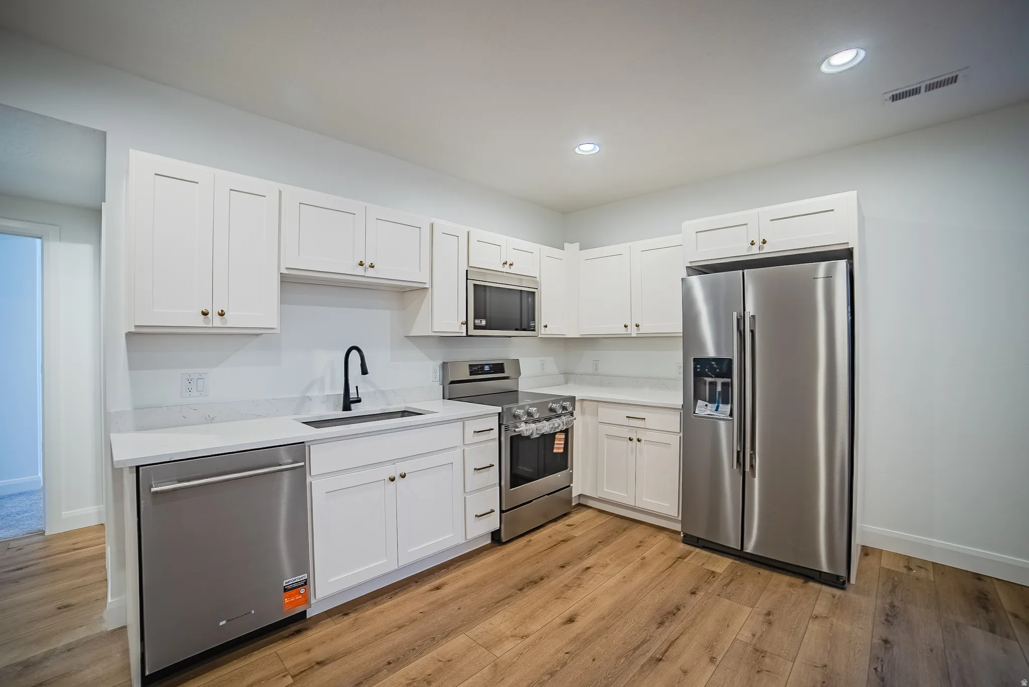 Modern kitchen featuring white shaker cabinetry, stainless steel appliances, light-toned countertops, wood-finish flooring, and recessed lighting
