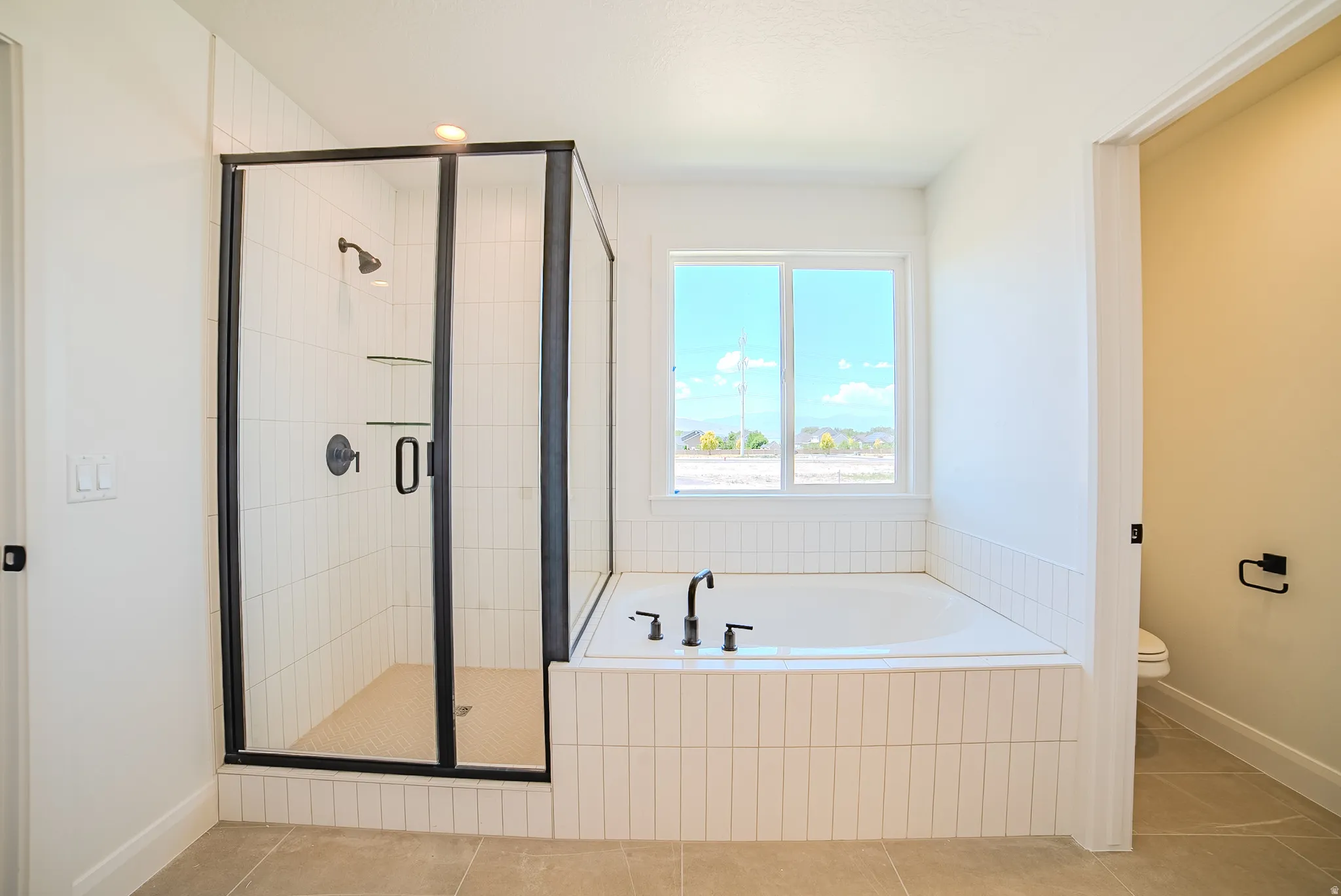 Contemporary bathroom featuring a walk-in shower with matte black fixtures, a soaking tub with coordinating matte black faucet, and vertical tile detailing