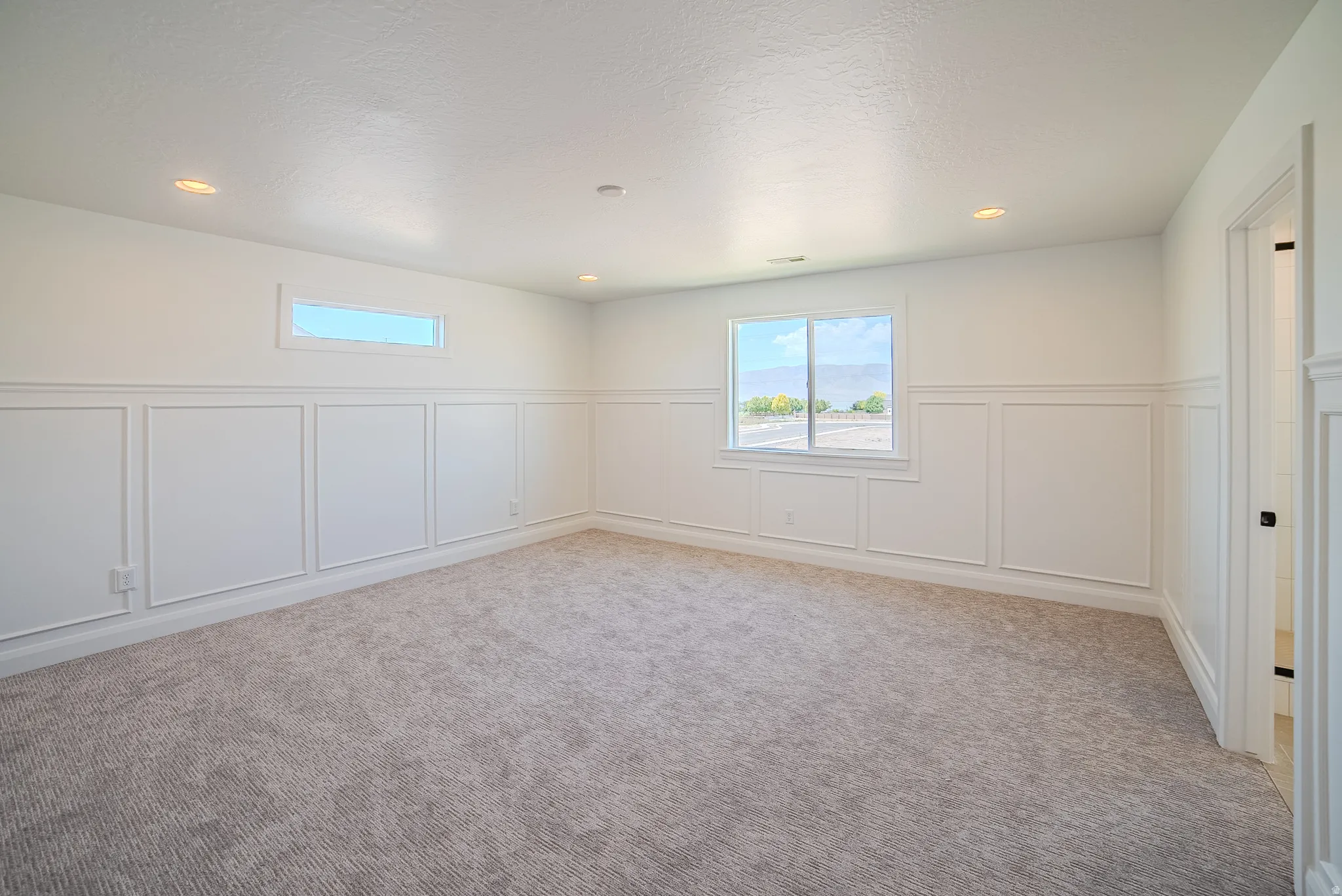 Spacious room featuring wainscoting paneling, recessed lighting, and soft gray carpeting