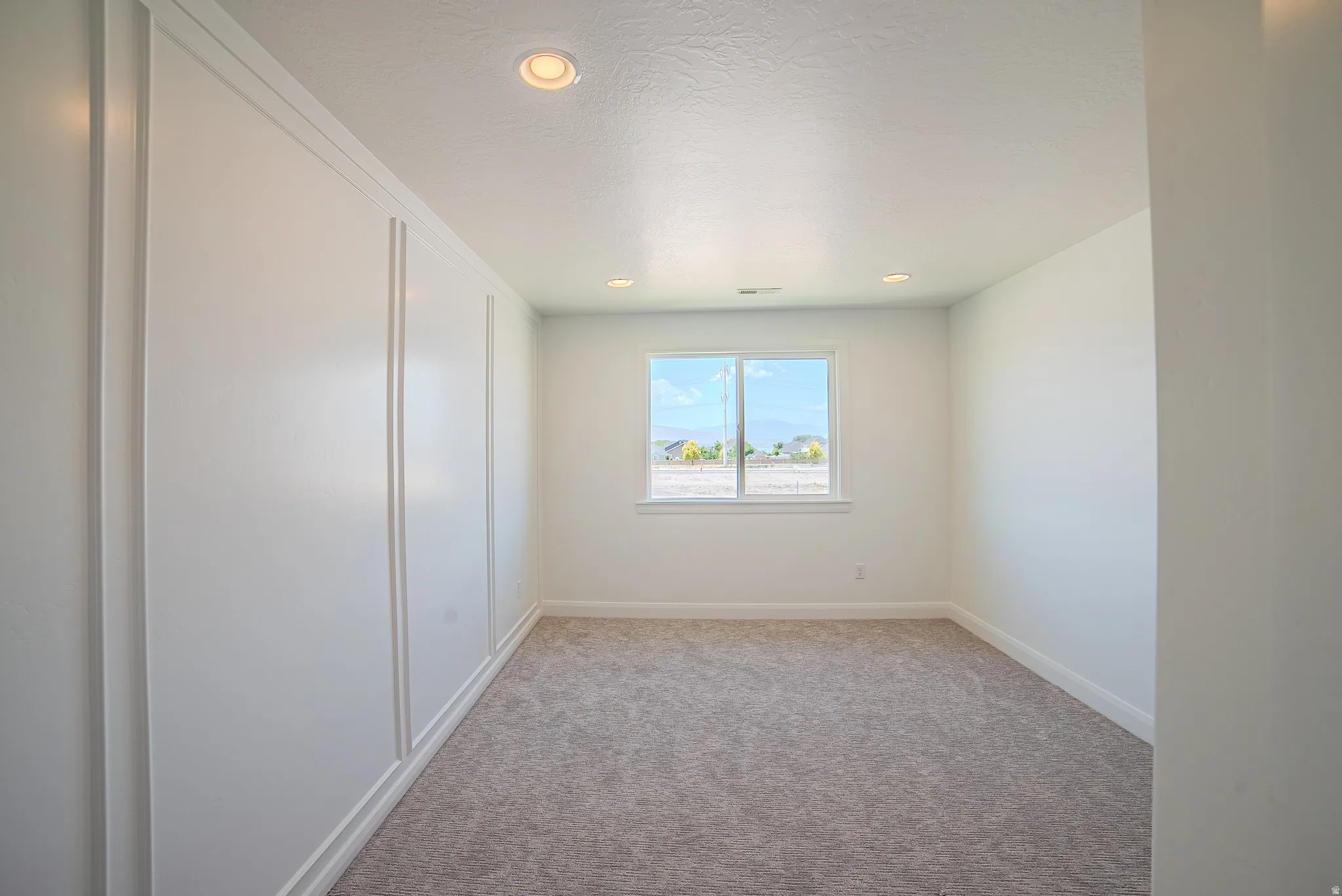 Spacious room featuring board and batten accent wall, recessed lighting, and a neutral carpeted floor
