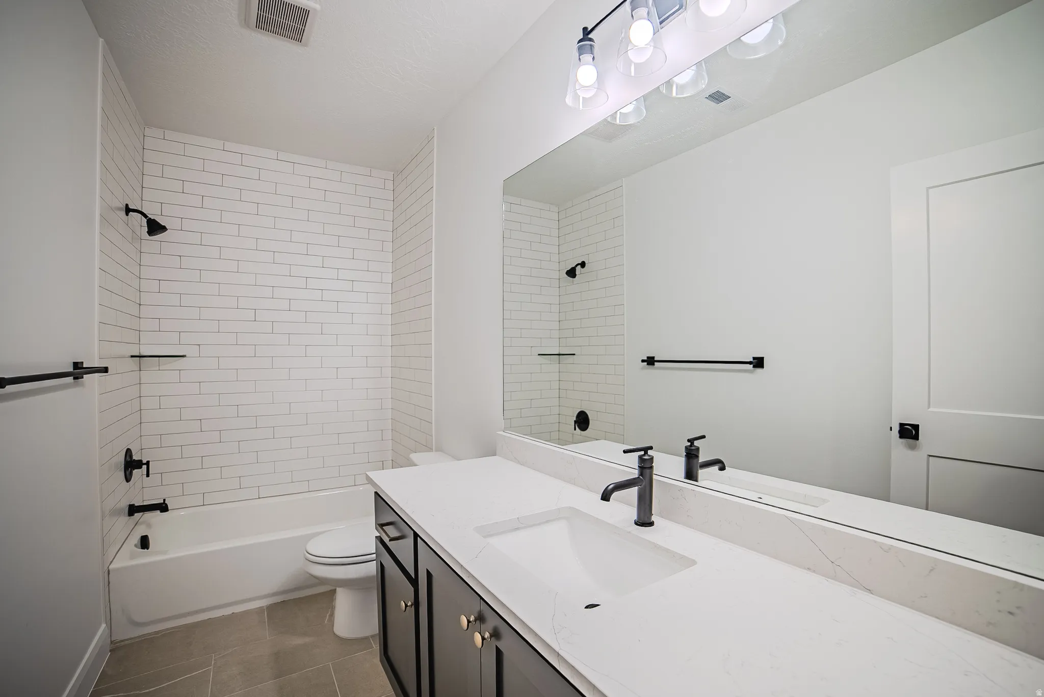 Bathroom featuring a white subway tile shower surround, a built-in tub, a vanity with a white countertop and integrated sink, matte black fixtures, and a large wall-mounted mirror