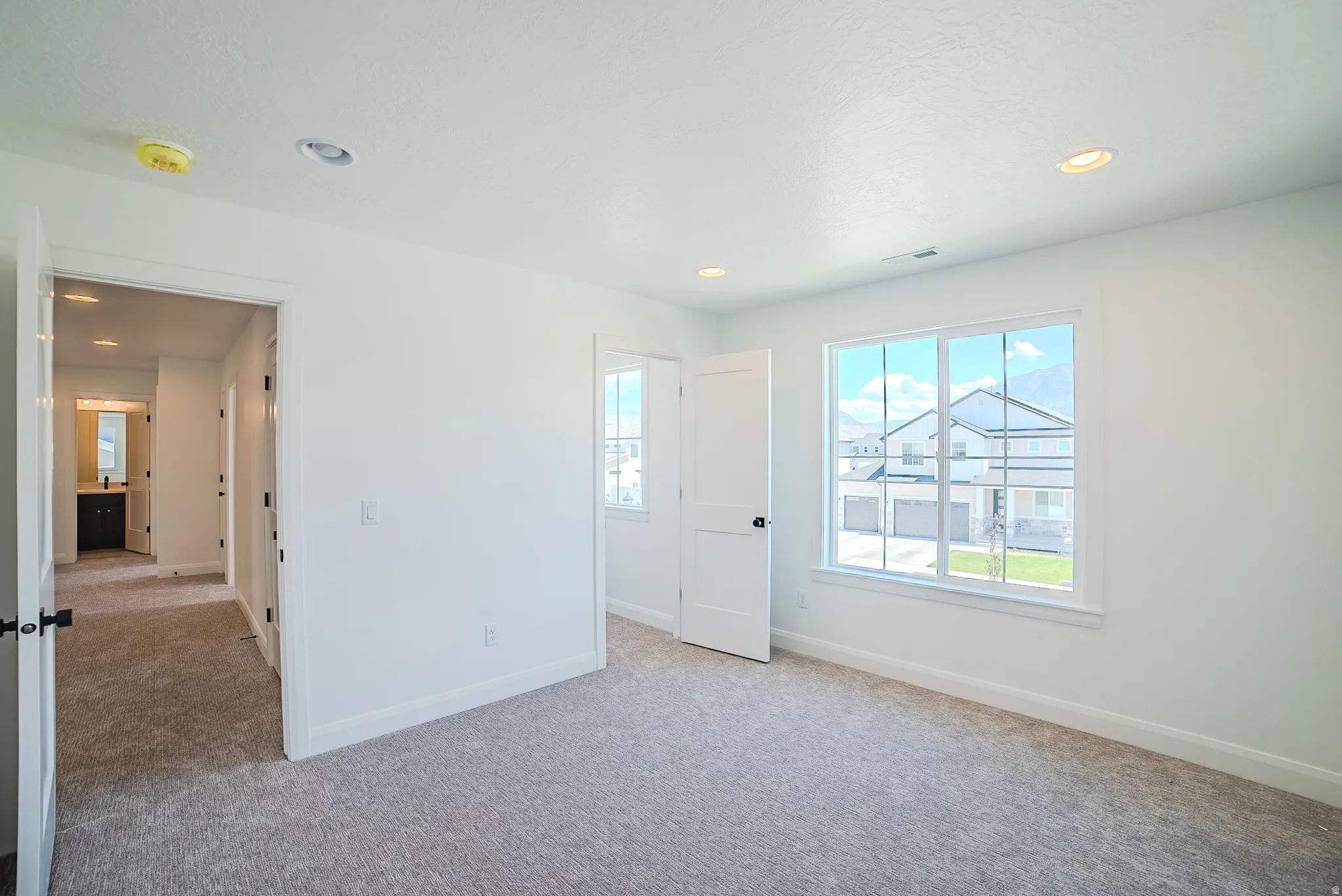 Spacious room featuring light gray carpet flooring, white walls, and a large multi-pane window