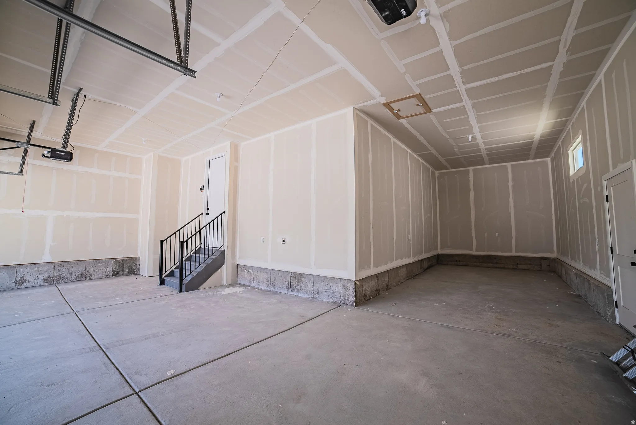 Spacious two-car garage featuring a concrete floor, high ceilings, and a staircase with black metal railings
