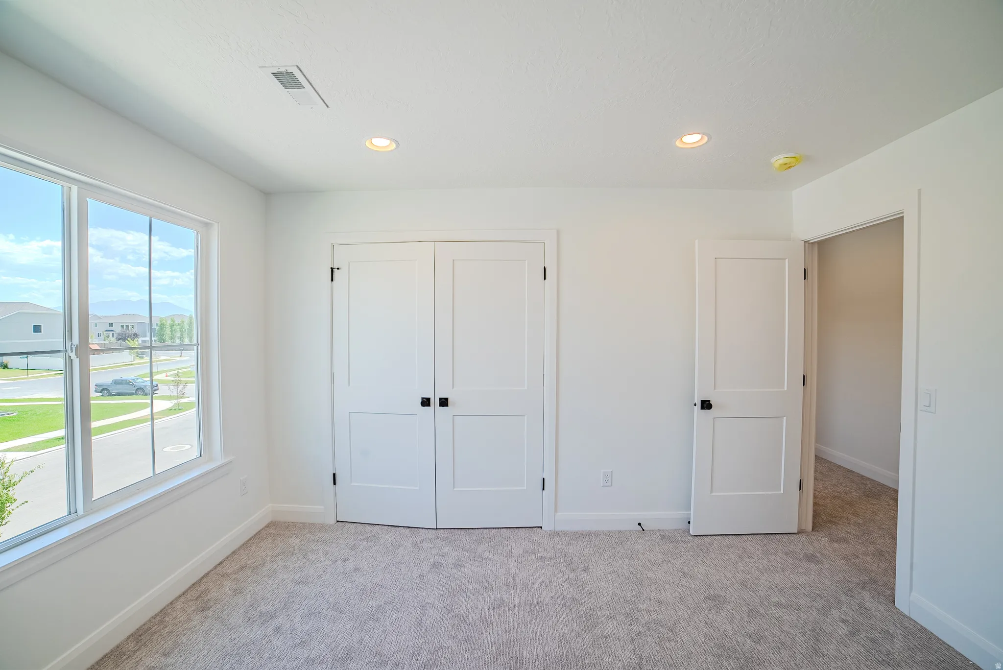 Spacious room featuring a large window, light-toned carpet, two panel doors with matte black hardware, and recessed lighting