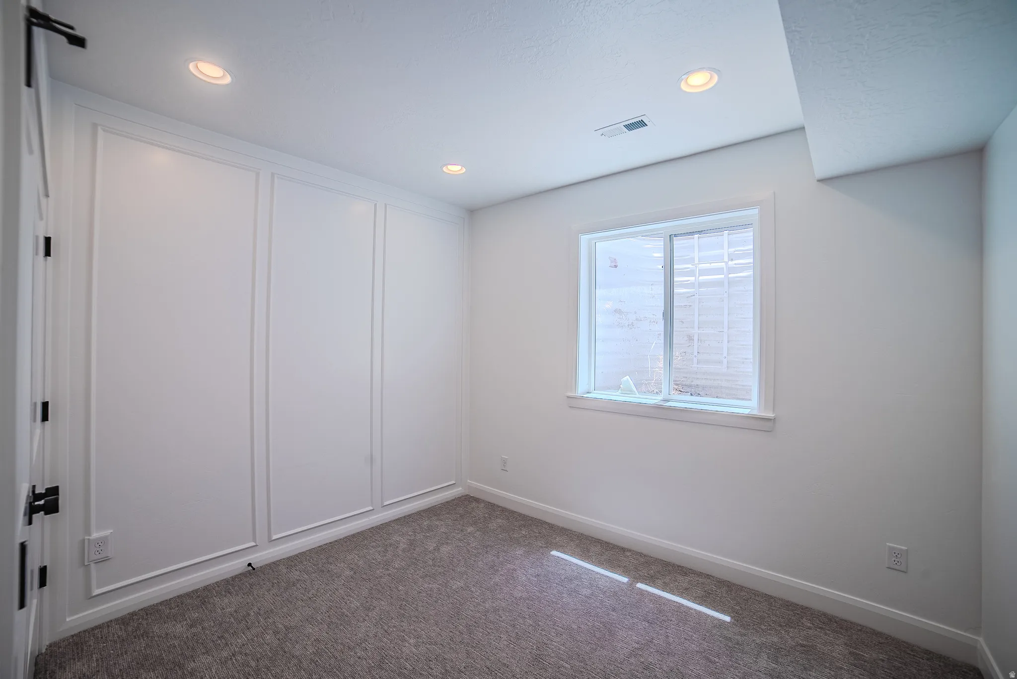 Bright interior space featuring recessed lighting, a window with exterior grating, and textured carpeting