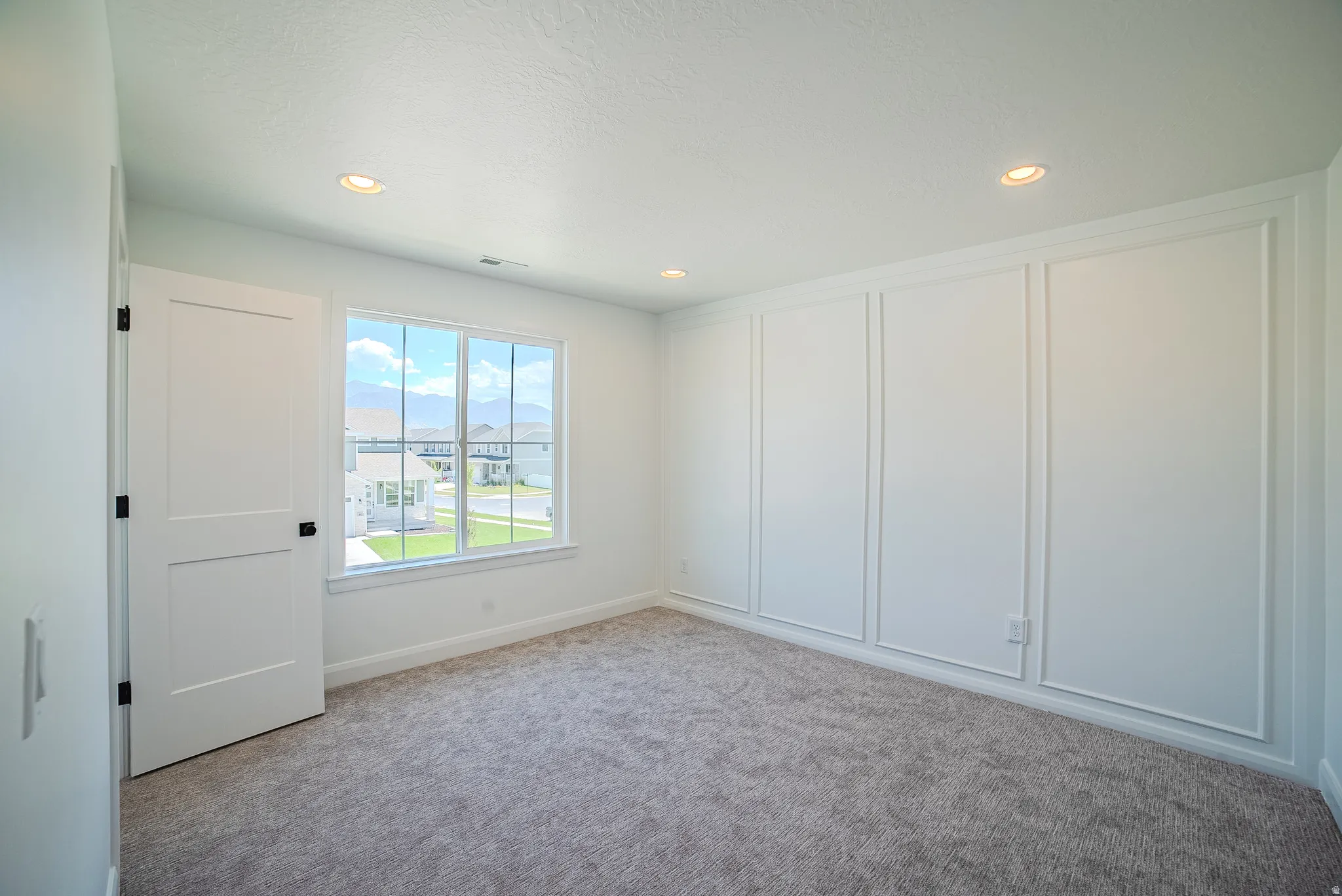 Interior room featuring a large window, plush gray carpet flooring, recessed lighting, white trim, and decorative wall paneling