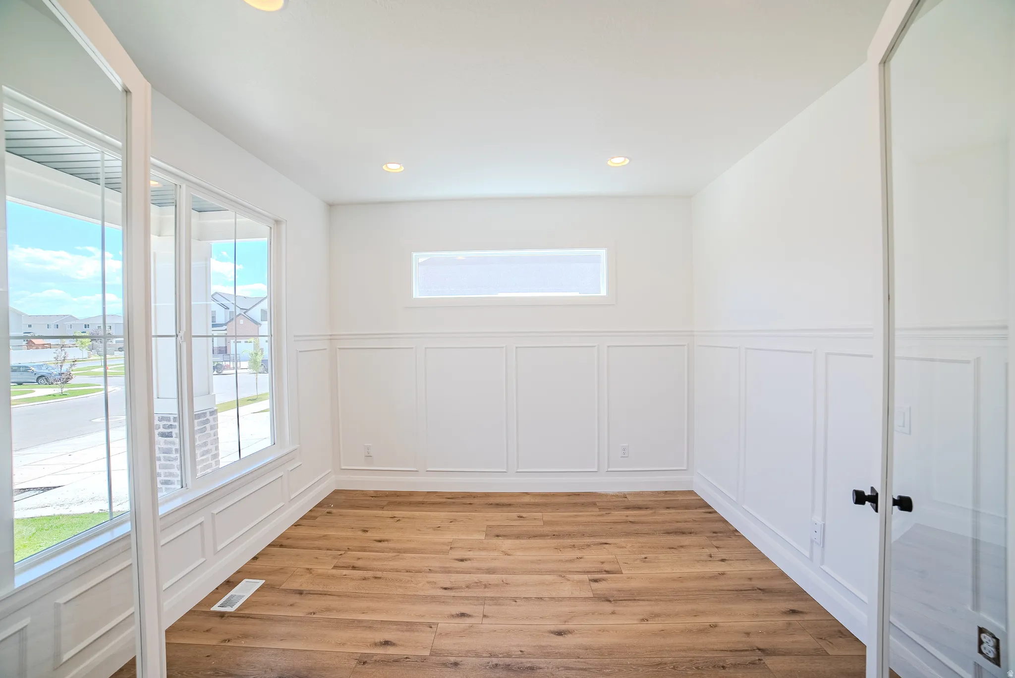 Room featuring wood-finish flooring, wainscoting, recessed lighting, and large windows