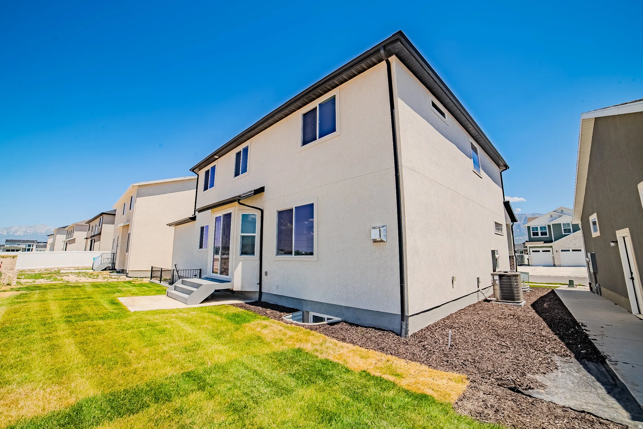 Rear exterior featuring a two-story design, stucco siding, multiple windows, a ground-level patio, and a grass lawn