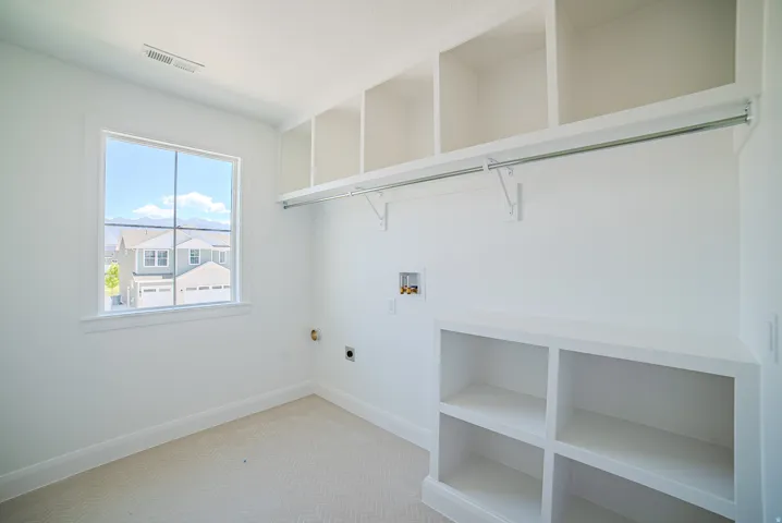 Bright utility room featuring a large window, extensive built-in shelving, a clothes hanging rod, and essential appliance hookups