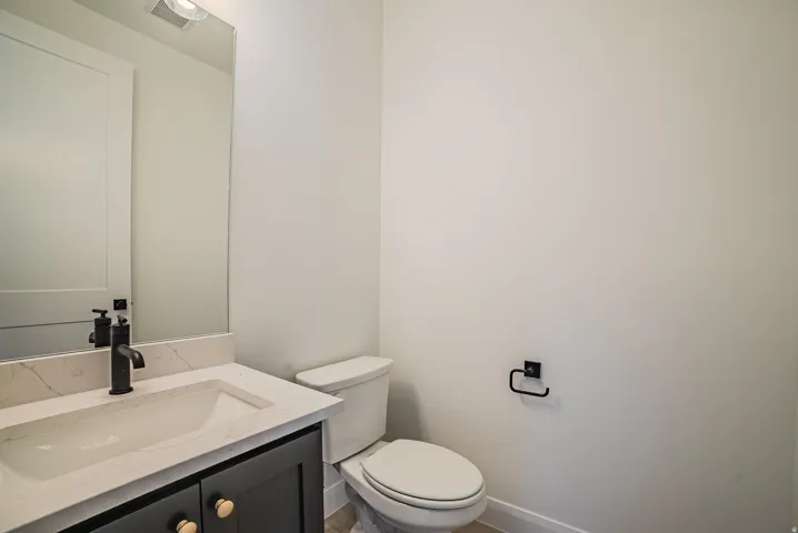 Modern bathroom featuring a dark grey vanity with gold-tone hardware, an integrated sink with a light-toned countertop, a black faucet, and a wall-mounted mirror