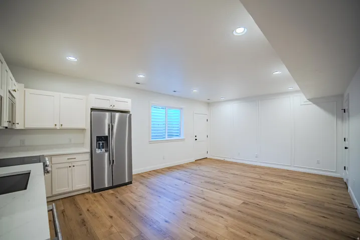 Open-concept living space featuring wood-finish flooring, recessed lighting, and a kitchen area with white cabinetry, a stainless steel refrigerator, and light-toned countertops